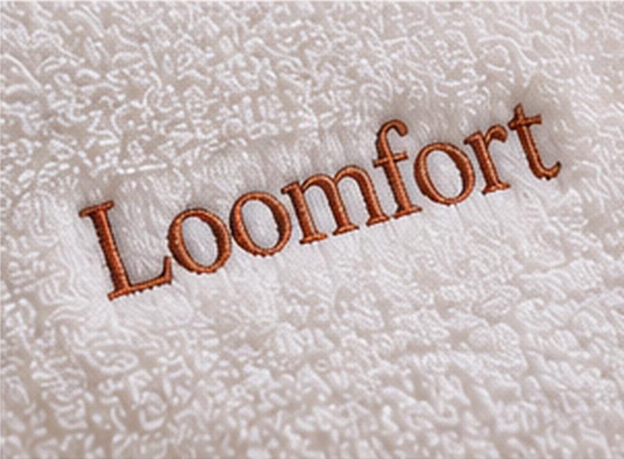 Macro stitch detail of a restrained terracotta monogram embroidered on white terry.