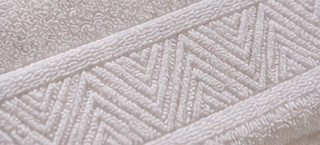 Macro detail of a white towel with a subtle tone-on-tone woven jacquard border.
